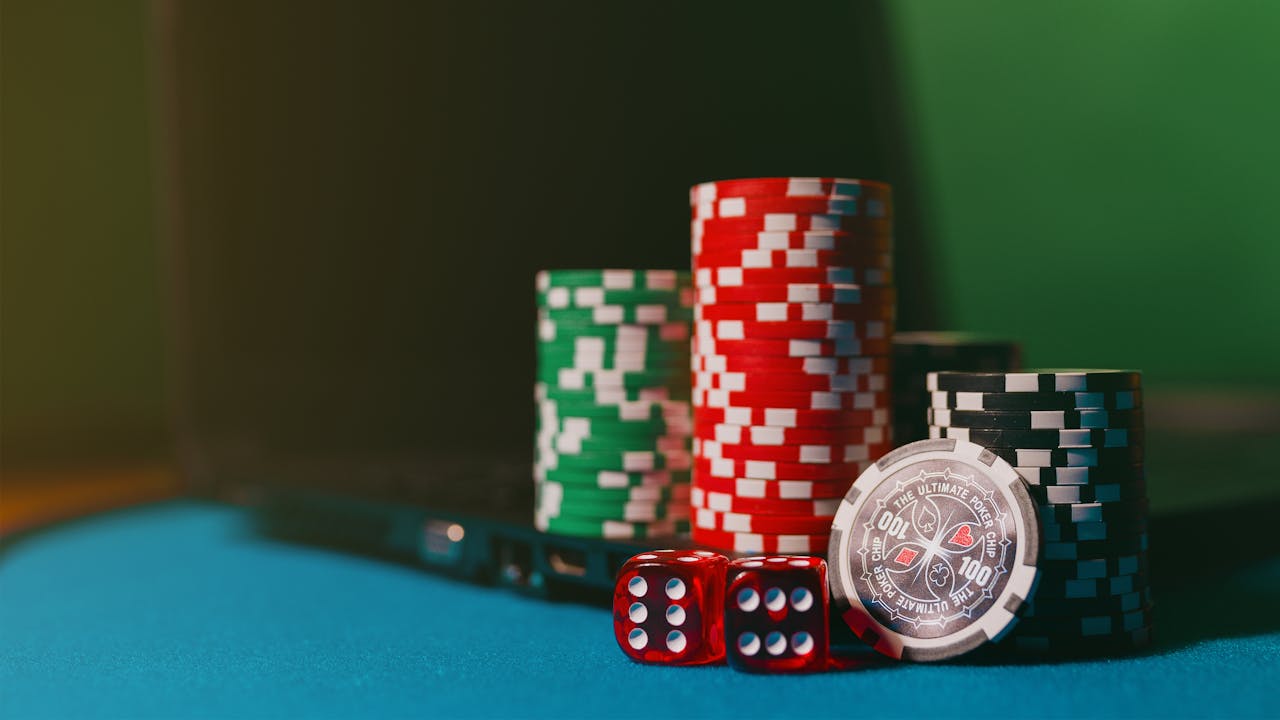 Close-up of casino chips and dice on a felt table, next to a laptop for online gambling.